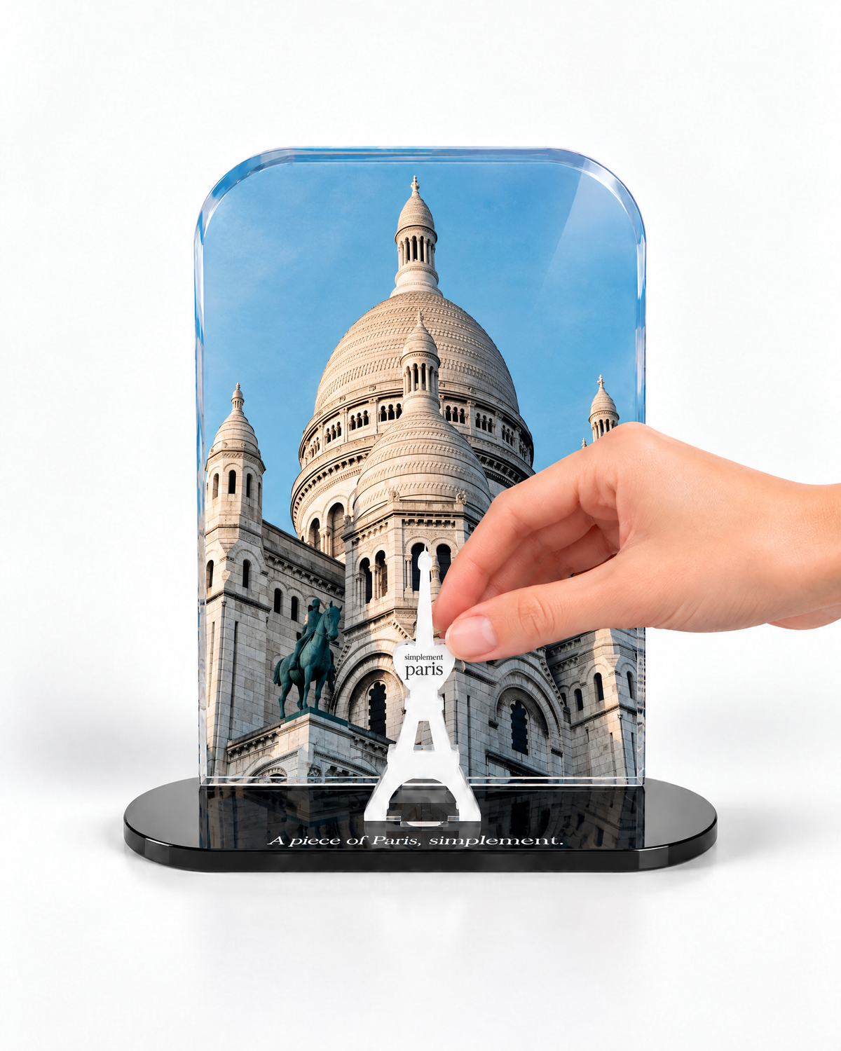 A hand placing the white signature Eiffel Tower in front of the Sacré-Cœur acrylic panel