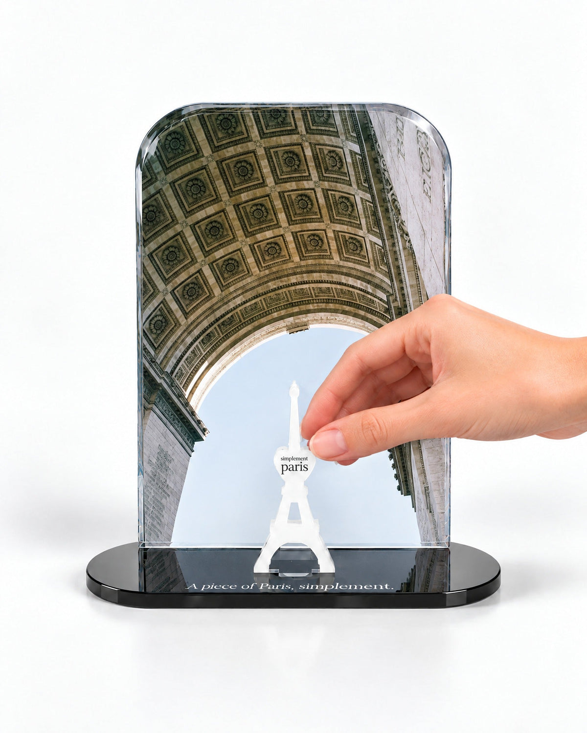 A hand placing the white signature Eiffel Tower in front of the Arc de Triomphe acrylic panel