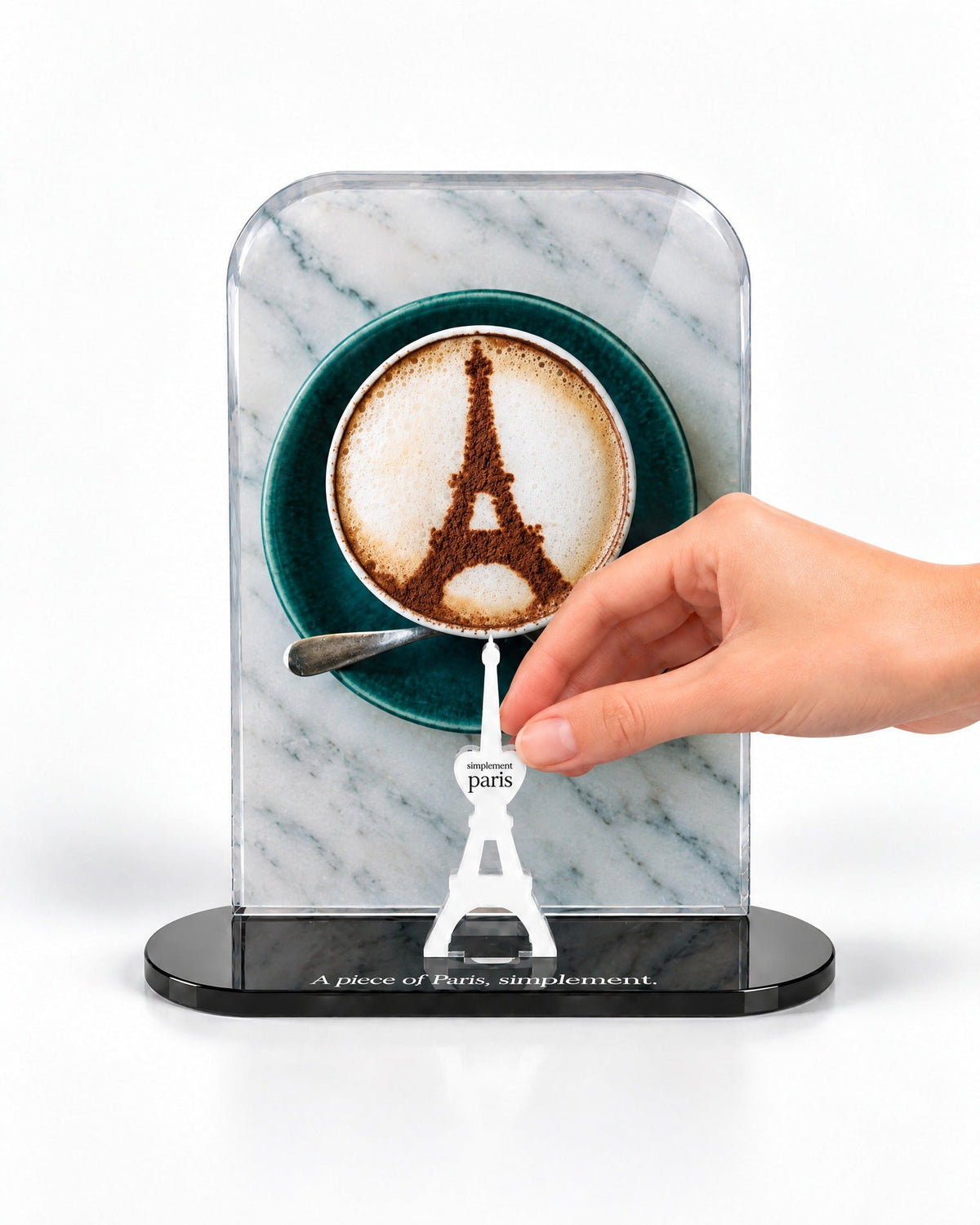 A hand placing the white signature Eiffel Tower in front of the Café Eiffel acrylic panel
