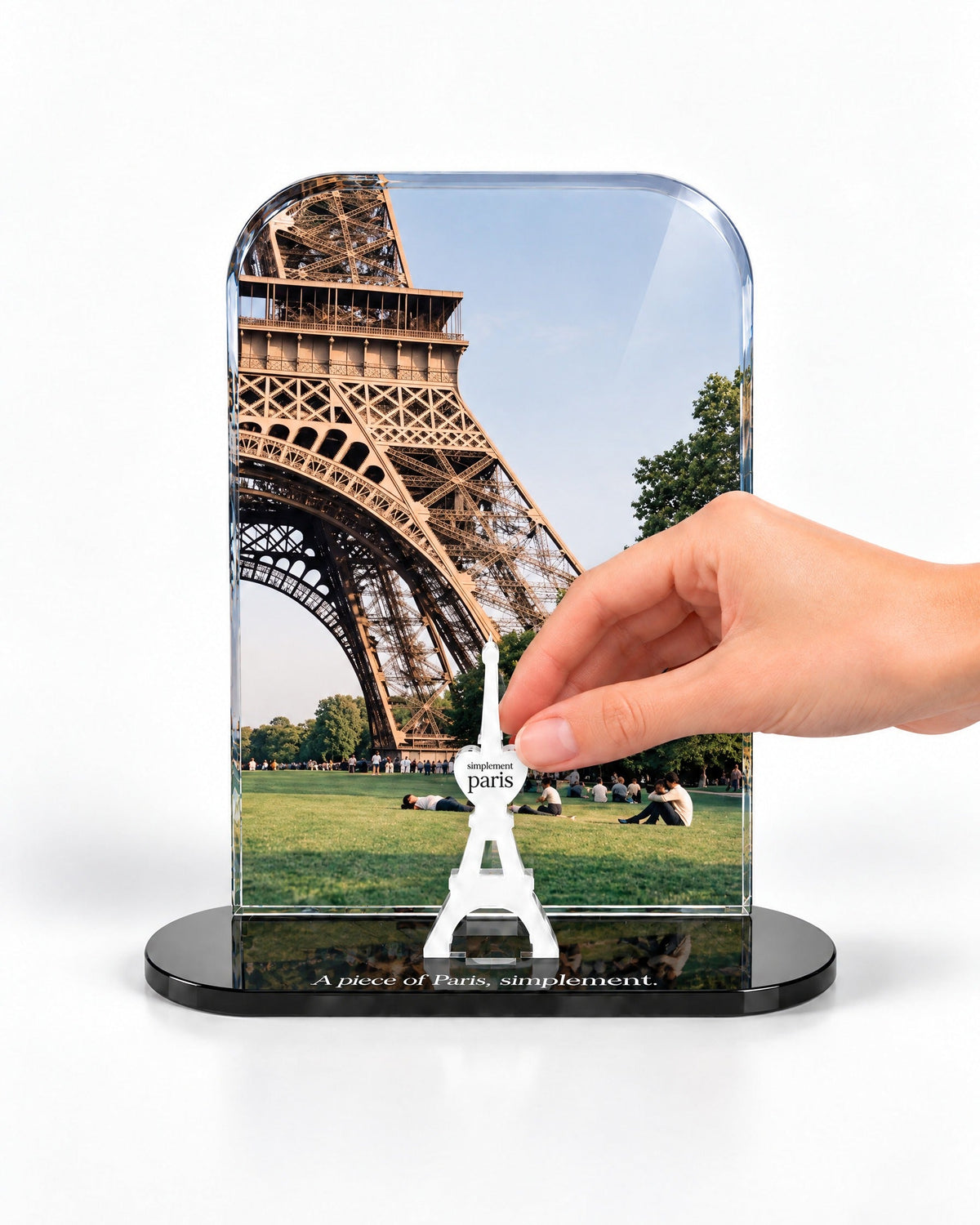 A hand placing the white signature Eiffel Tower in front of the Champ de Mars acrylic panel