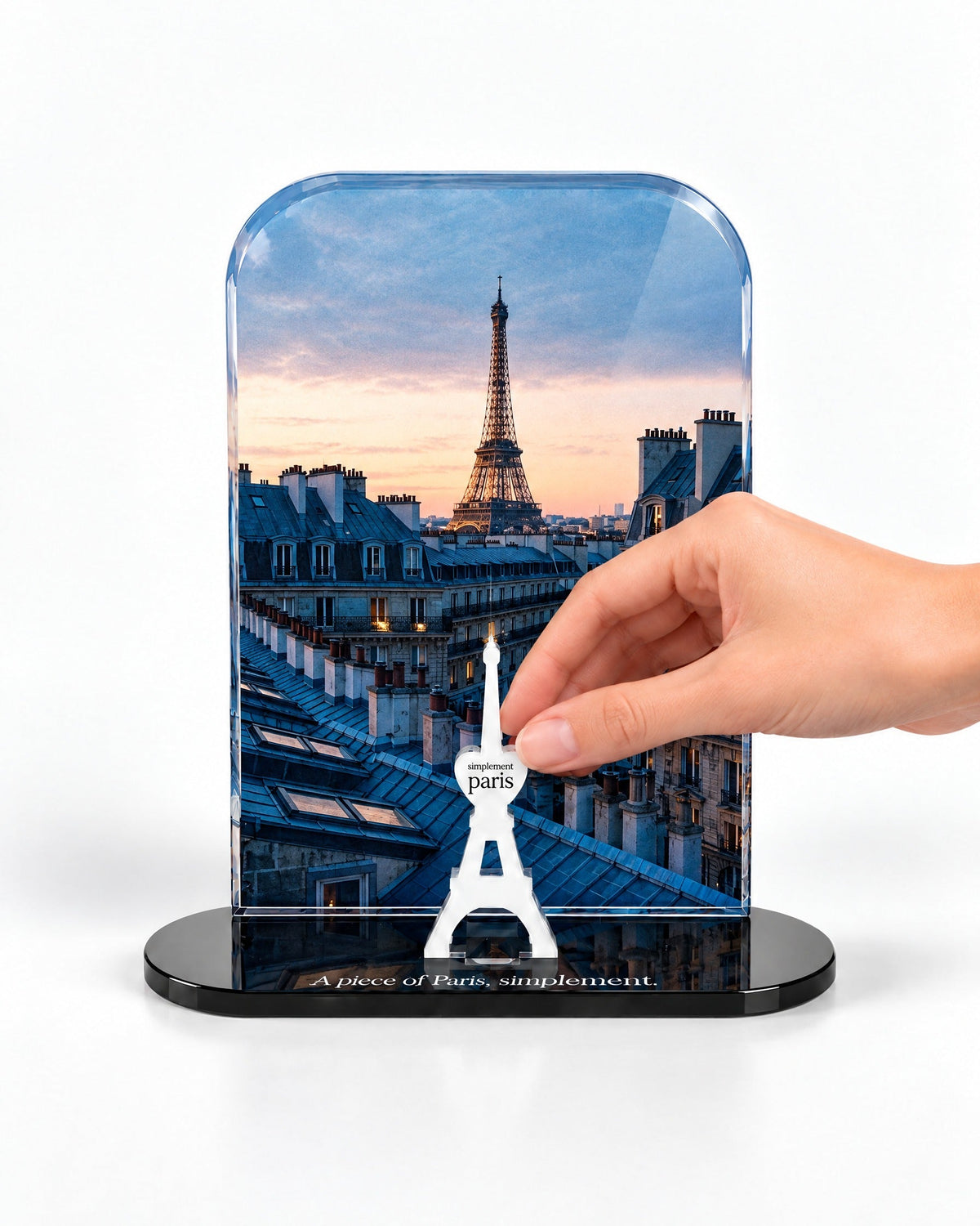 A hand placing the white signature Eiffel Tower in front of the Eiffel at Dusk acrylic panel