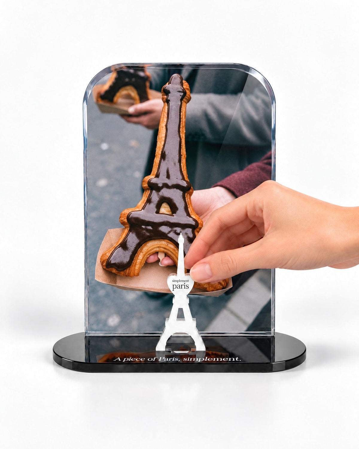 A hand placing the white signature Eiffel Tower in front of the Eiffel Croissant acrylic panel