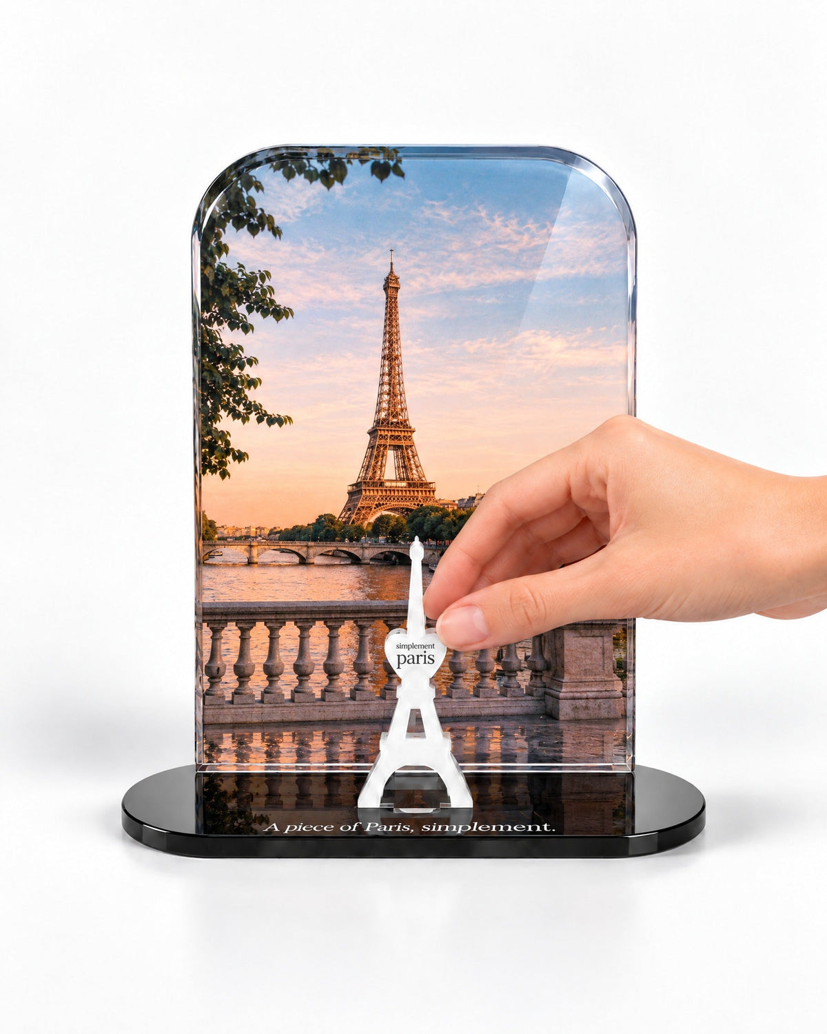 A hand placing the white signature Eiffel Tower in front of the Eiffel Sunset acrylic panel