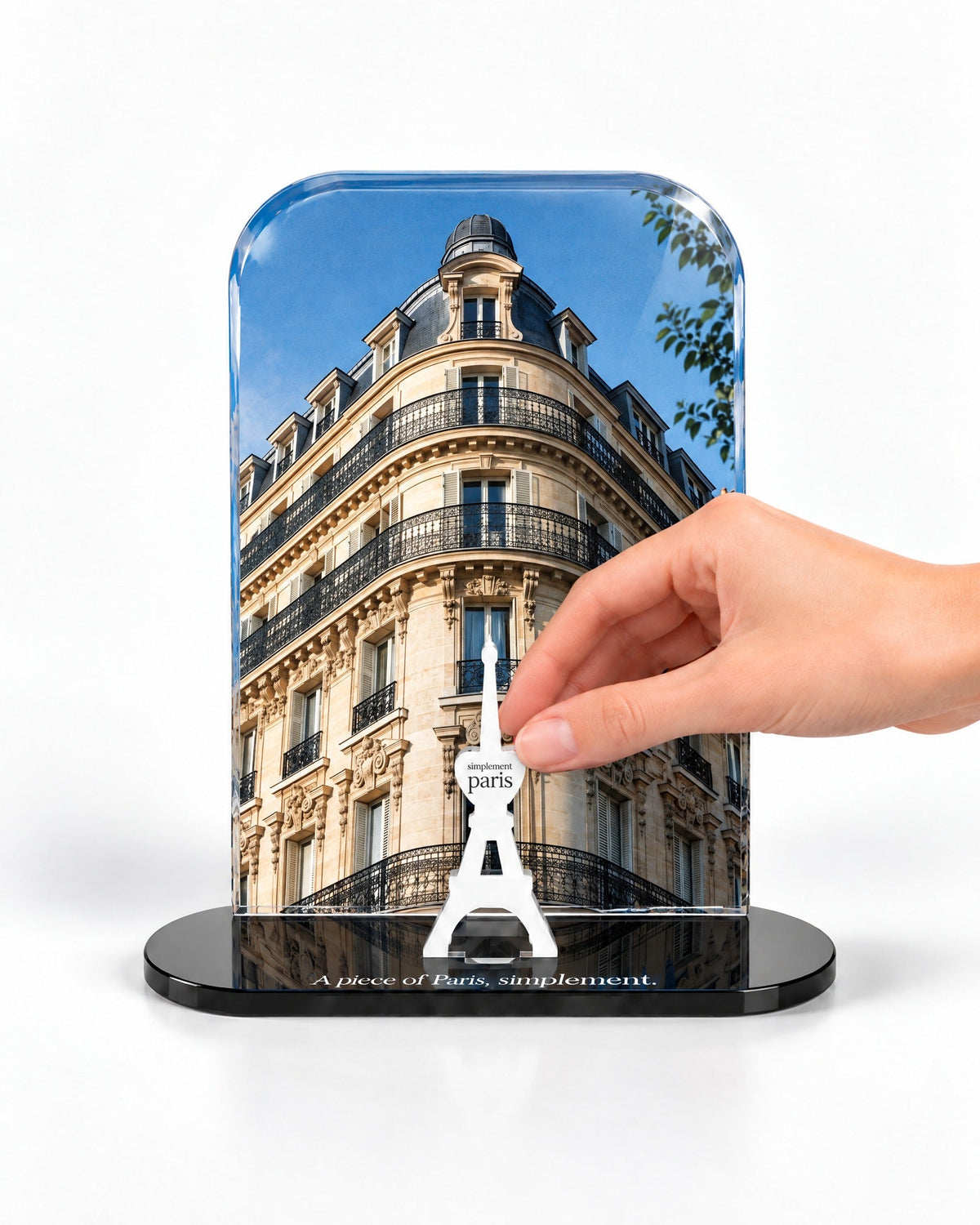 A hand placing the white signature Eiffel Tower in front of the Haussmann acrylic panel
