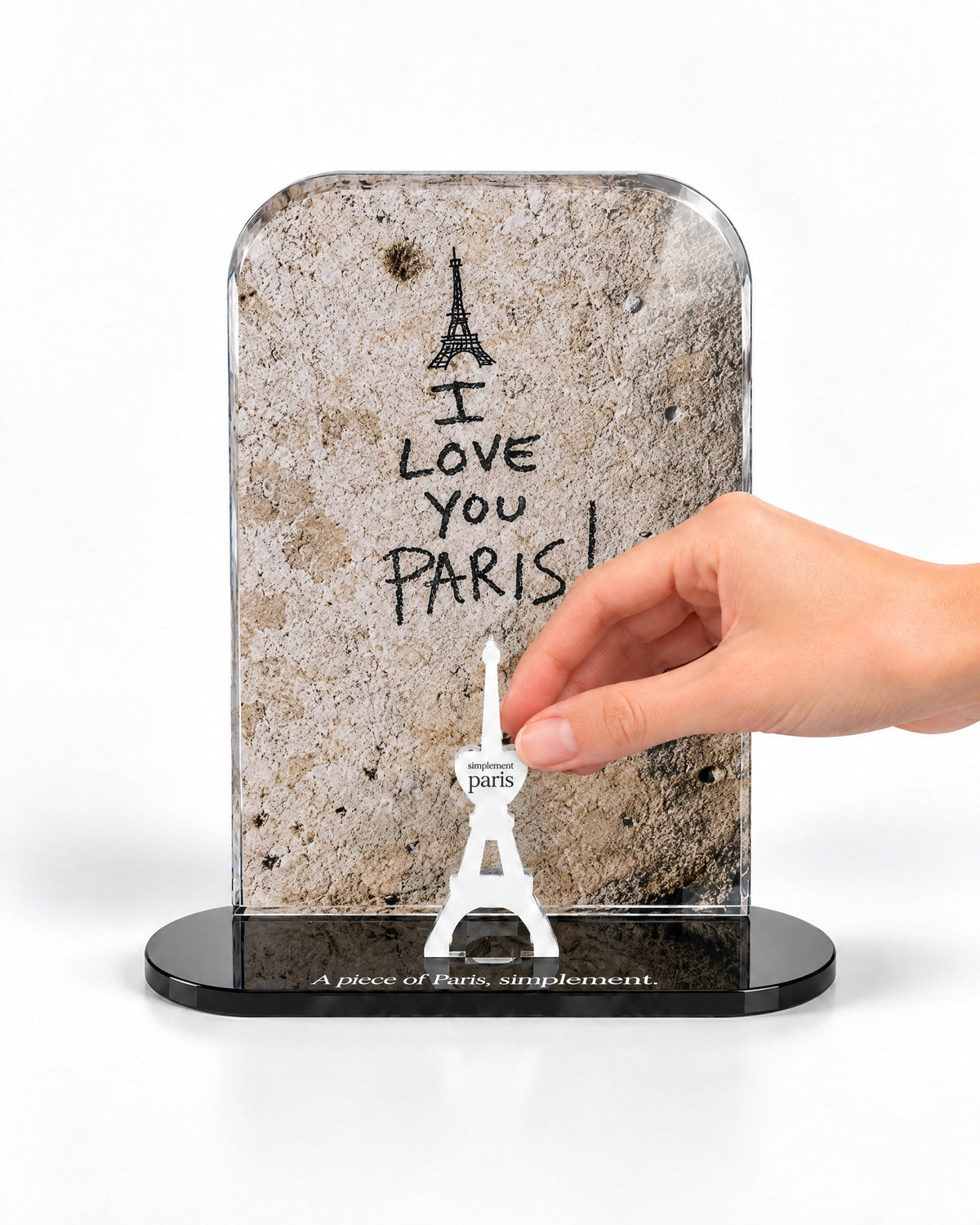 A hand placing the white signature Eiffel Tower in front of the I Love You Paris acrylic panel