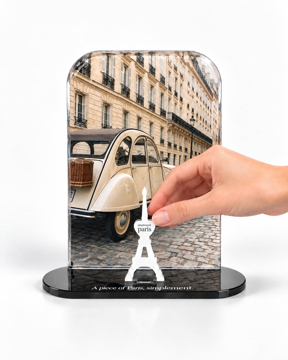 A hand placing the white signature Eiffel Tower in front of the La Deux Chevaux acrylic panel