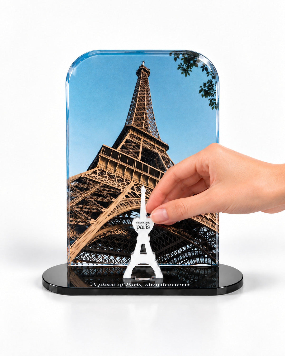 A hand placing the white signature Eiffel Tower in front of the La Tour Eiffel acrylic panel