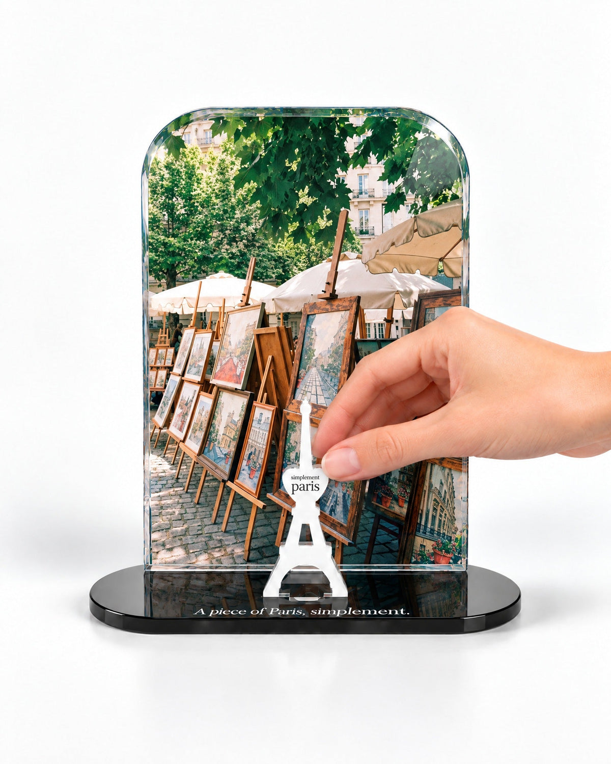 A hand placing the white signature Eiffel Tower in front of the Les Artistes acrylic panel