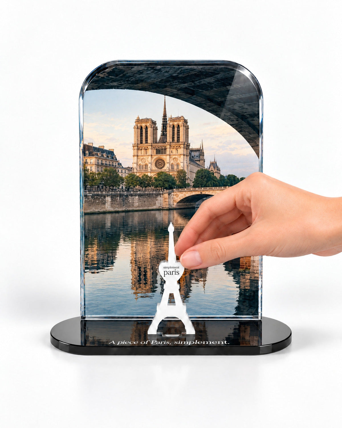 A hand placing the white signature Eiffel Tower in front of the Notre-Dame acrylic panel