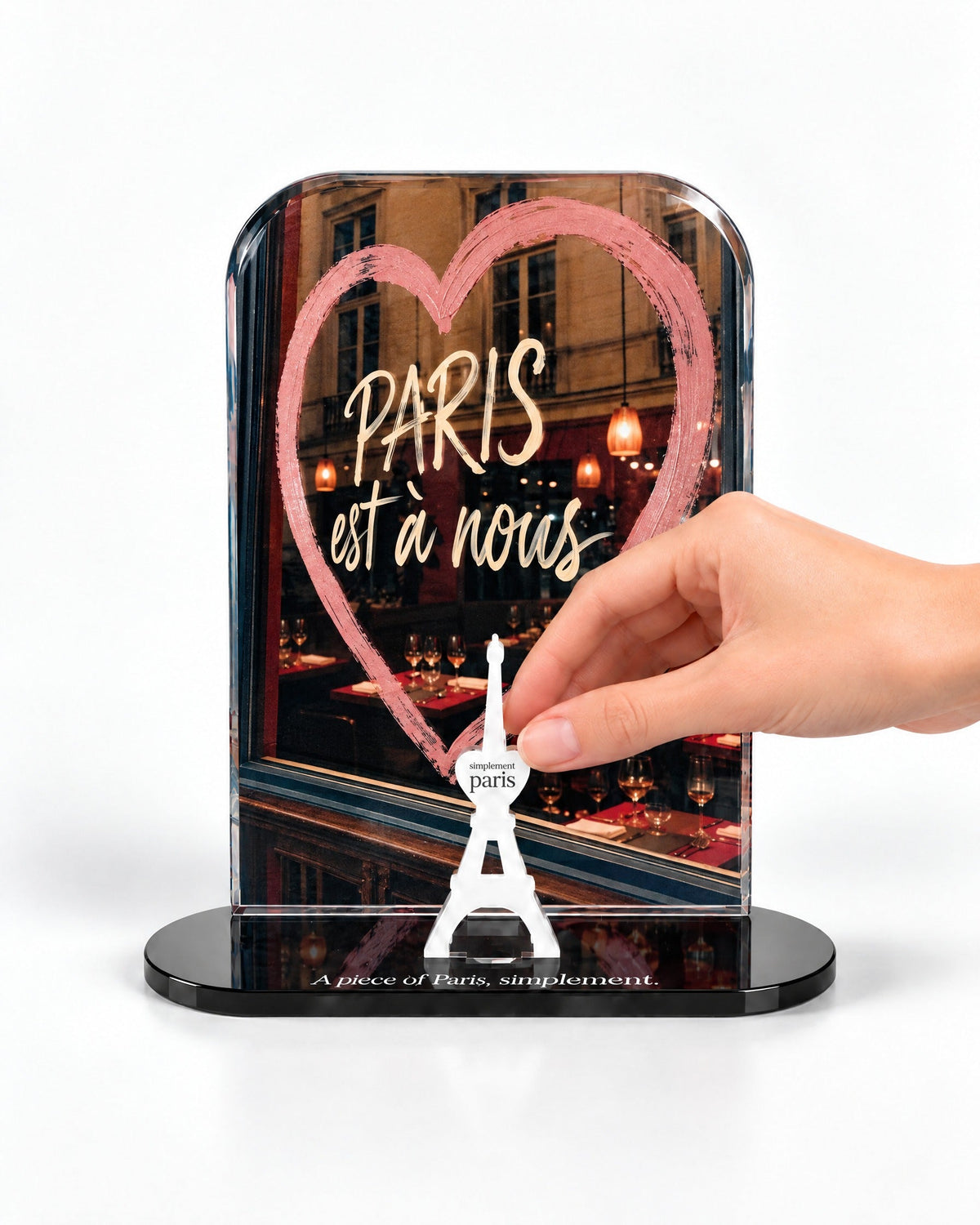 A hand placing the white signature Eiffel Tower in front of the Paris Est à Nous acrylic panel