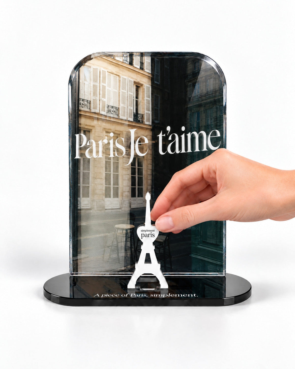 A hand placing the white signature Eiffel Tower in front of the Paris Je T'aime acrylic panel