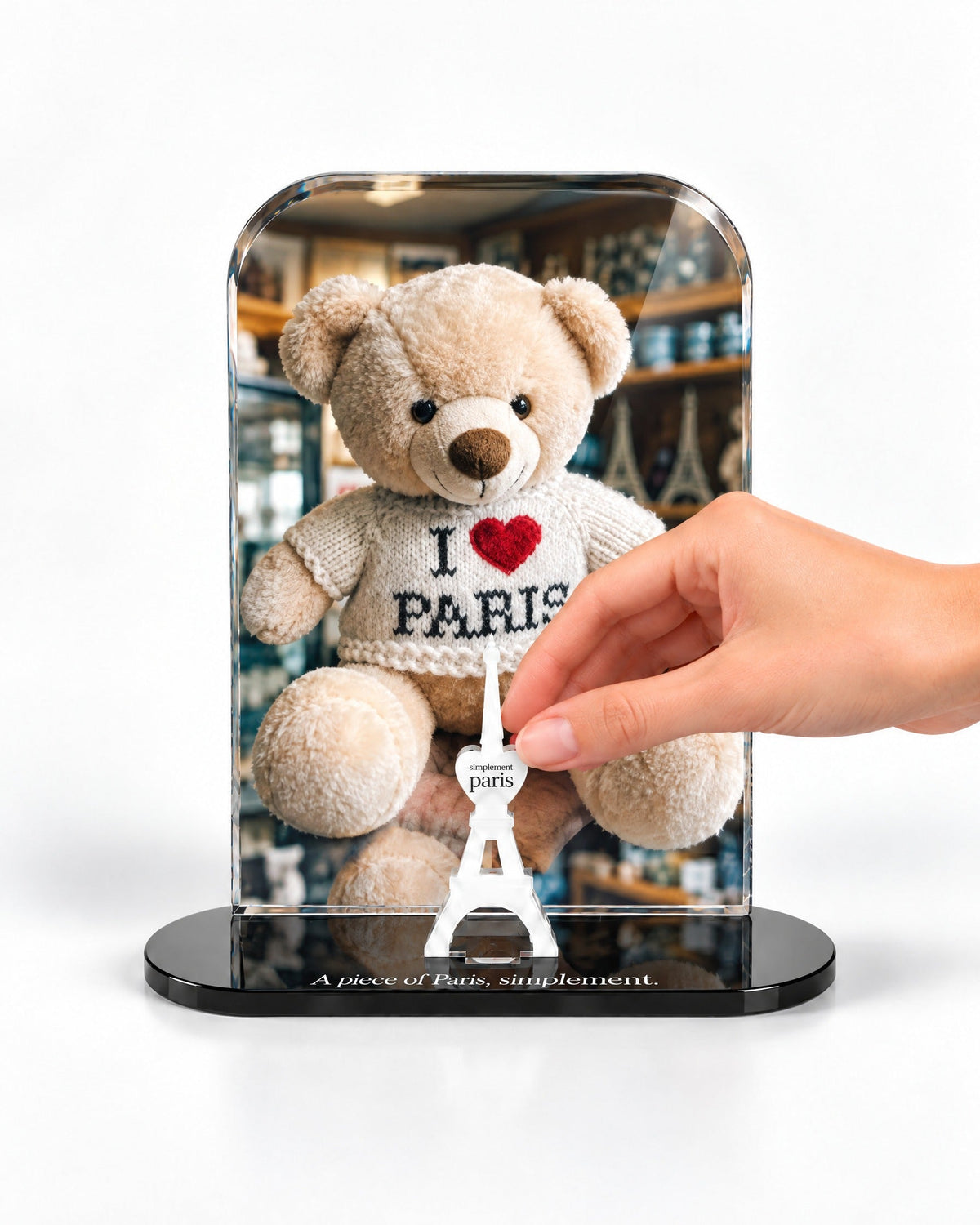 A hand placing the white signature Eiffel Tower in front of the Paris Teddy acrylic panel