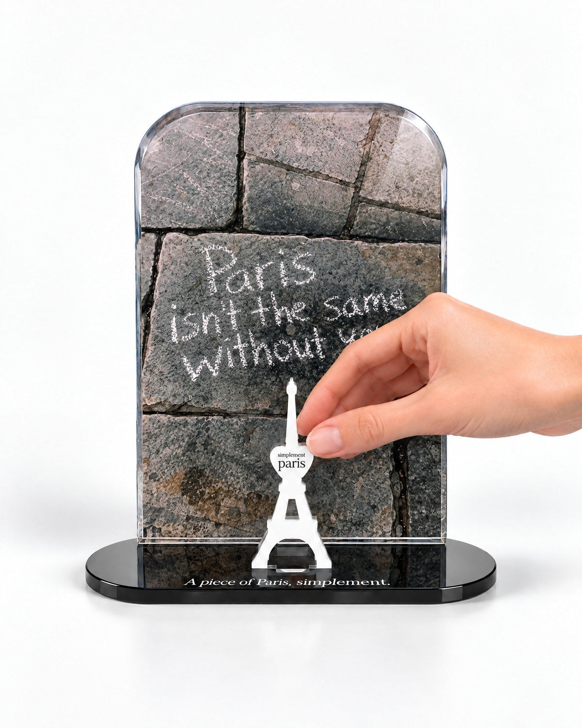 A hand placing the white signature Eiffel Tower in front of the Paris Without You acrylic panel