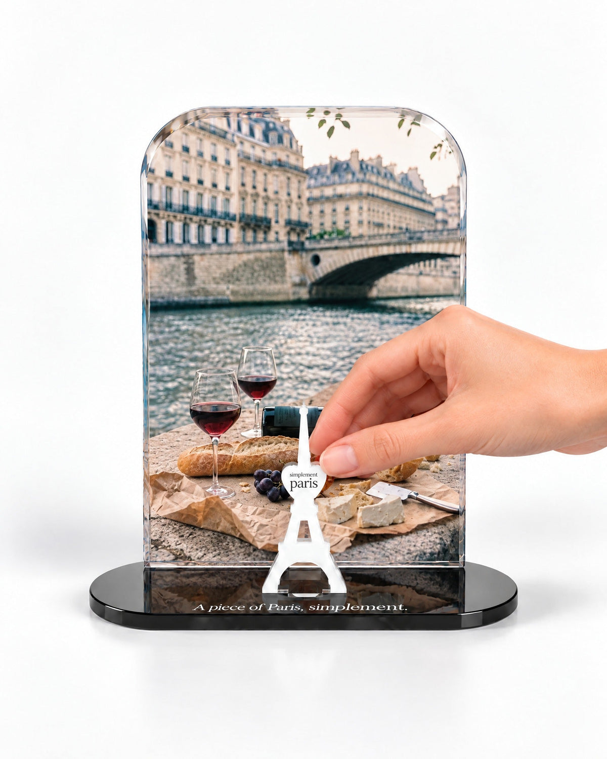 A hand placing the white signature Eiffel Tower in front of the Picnic on the Seine acrylic panel