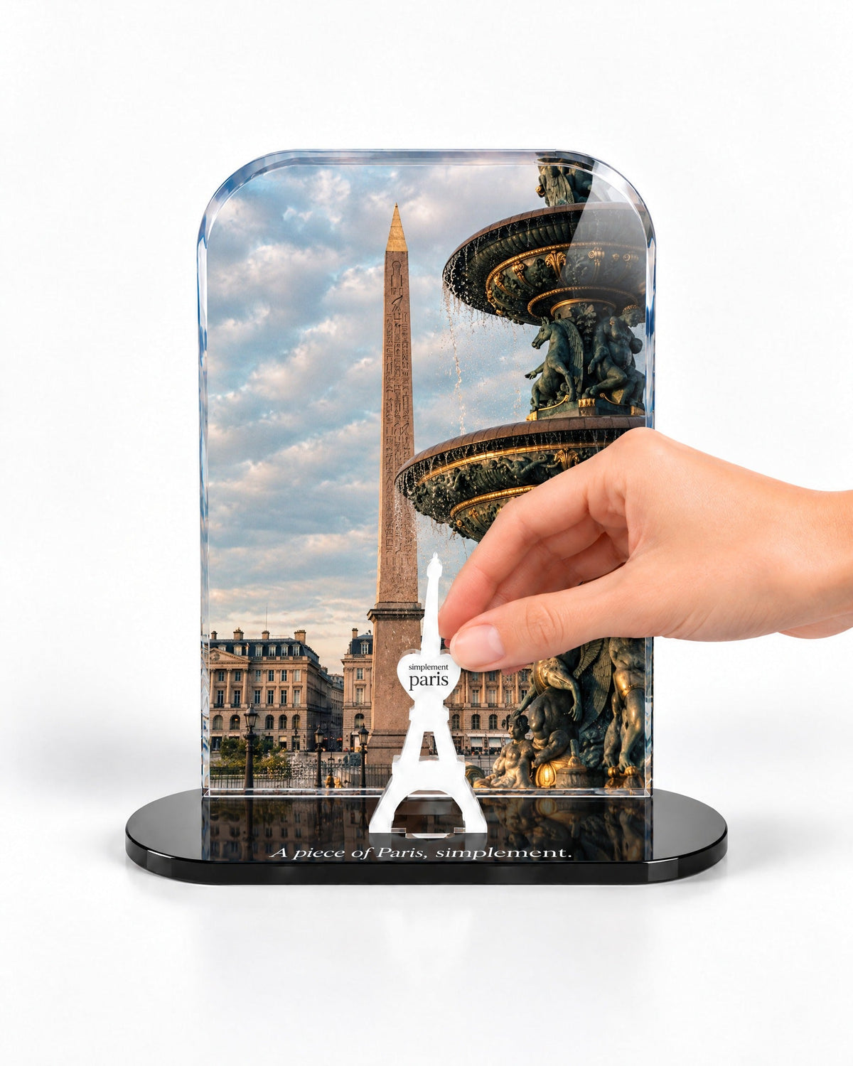 A hand placing the white signature Eiffel Tower in front of the Place de la Concorde acrylic panel