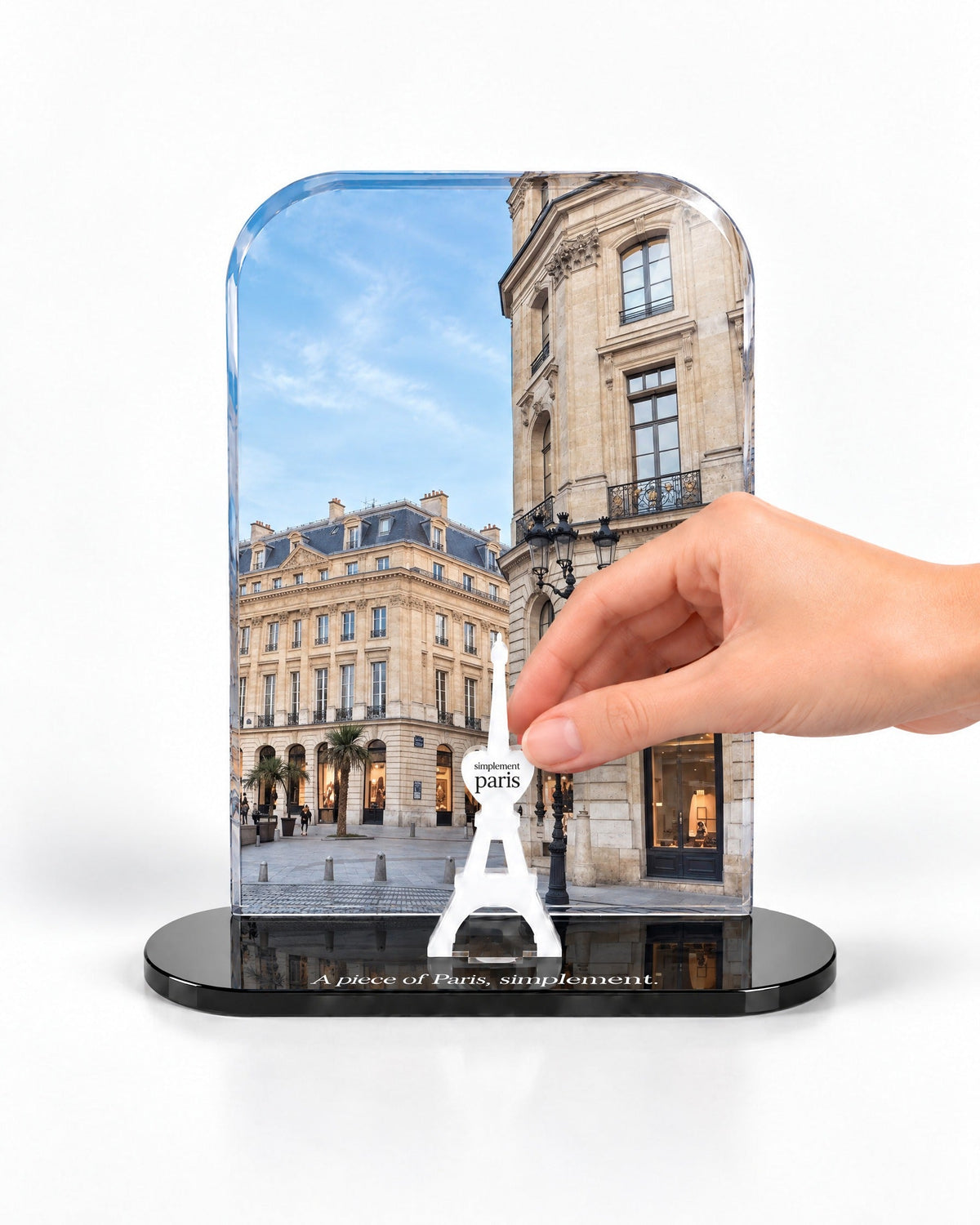 A hand placing the white signature Eiffel Tower in front of the Place Parisienne acrylic panel