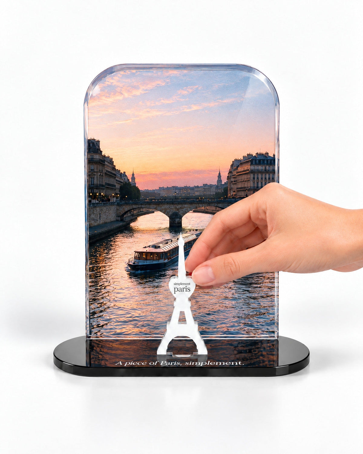 A hand placing the white signature Eiffel Tower in front of the Seine at Sunset acrylic panel