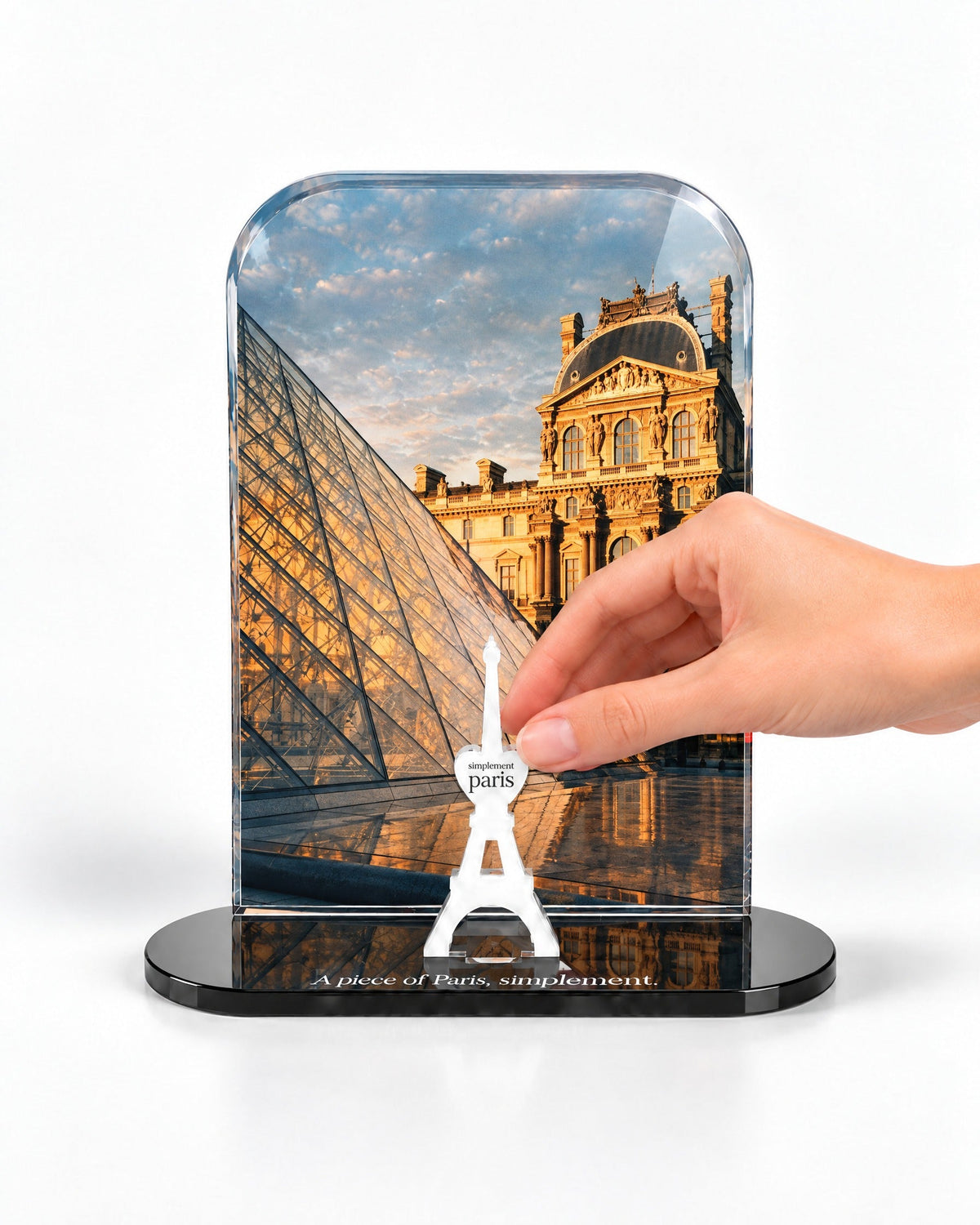 A hand placing the white signature Eiffel Tower in front of The Louvre acrylic panel