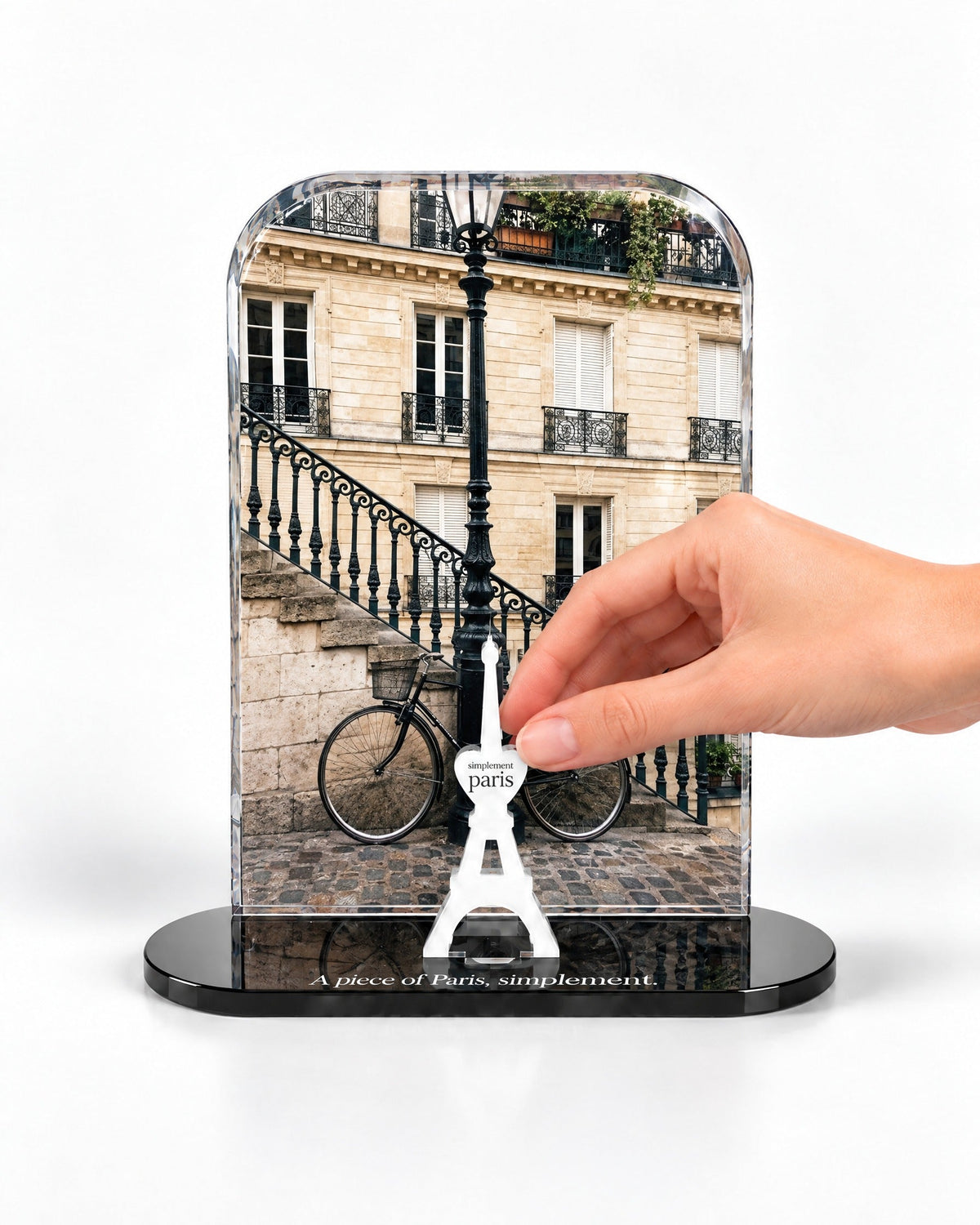 A hand placing the white signature Eiffel Tower in front of The Parisian Bicycle acrylic panel