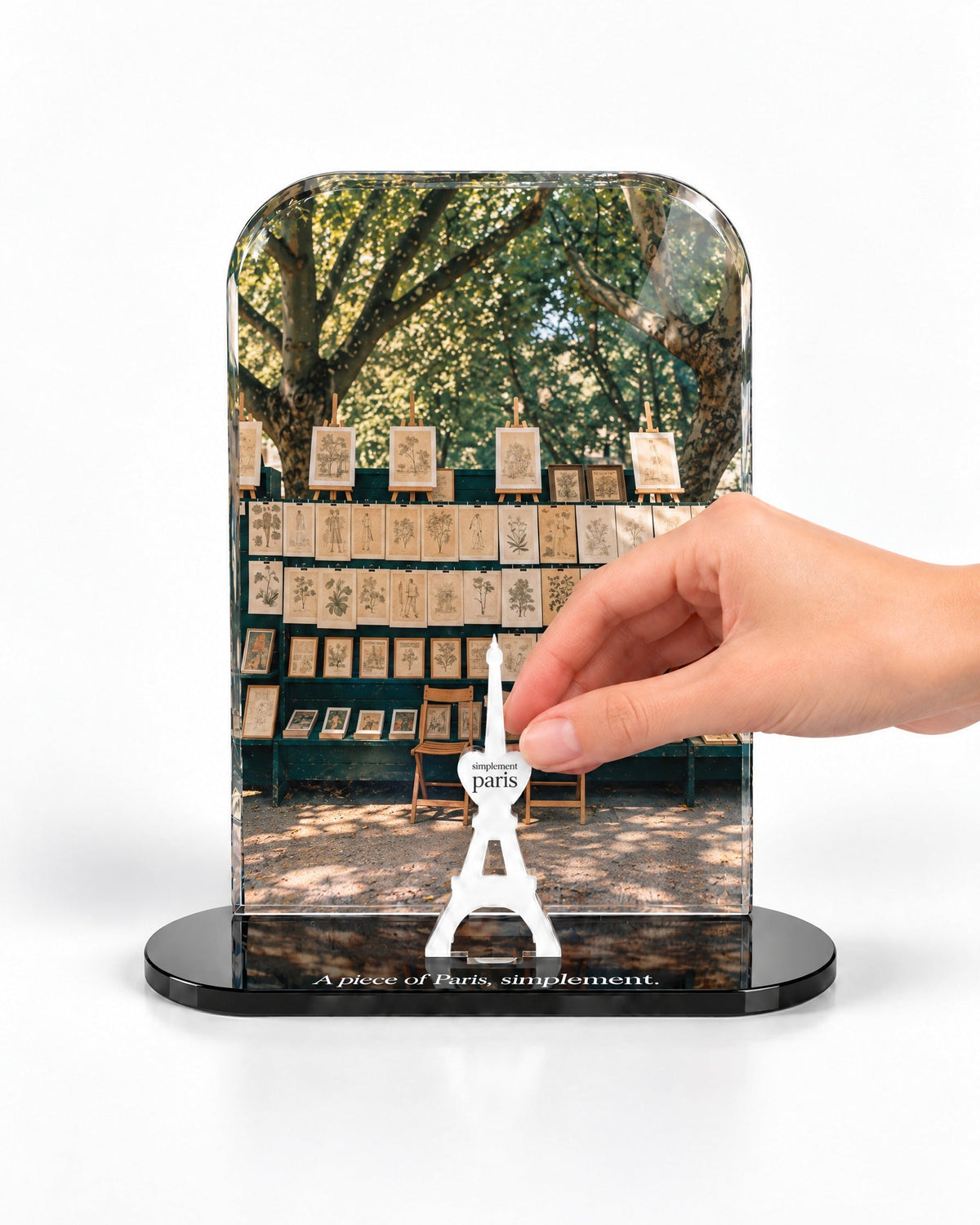 A hand placing the white signature Eiffel Tower in front of The Print Sellers acrylic panel