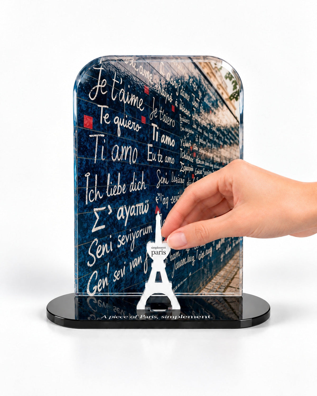 A hand placing the white signature Eiffel Tower in front of the Wall of Love acrylic panel